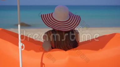 一位年轻<strong>女子坐在</strong>一张充气<strong>沙发上</strong>的热带海滩上的慢镜头。 暑假概念